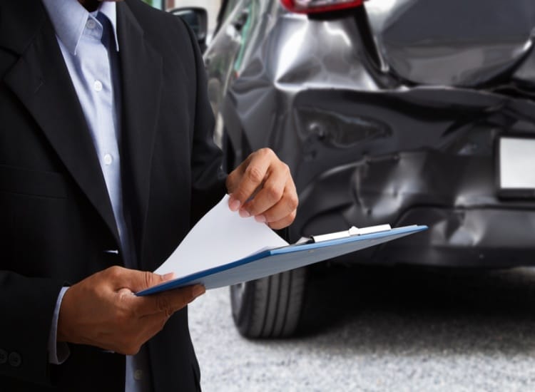 Insurance officer writing on clipboard while insurance agent examining black car after accident.